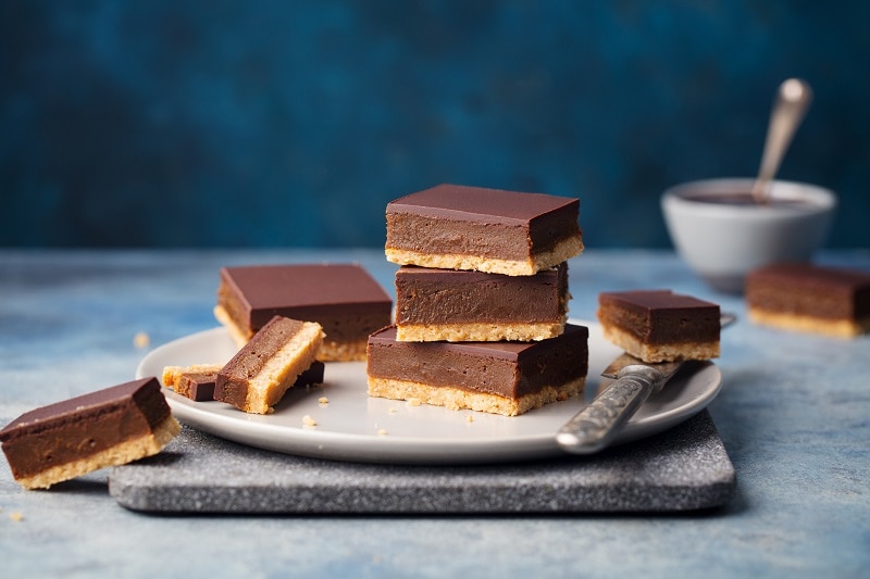 A Plate Holds a Stack of Millionaire Shortbread Slices With a Few Scattered Around the Plate.