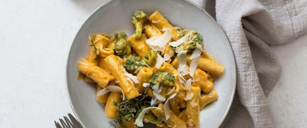 An Overhead View Shows Pumpkin Alfredo Sauce Over Penne and Broccoli in a White Bowl.