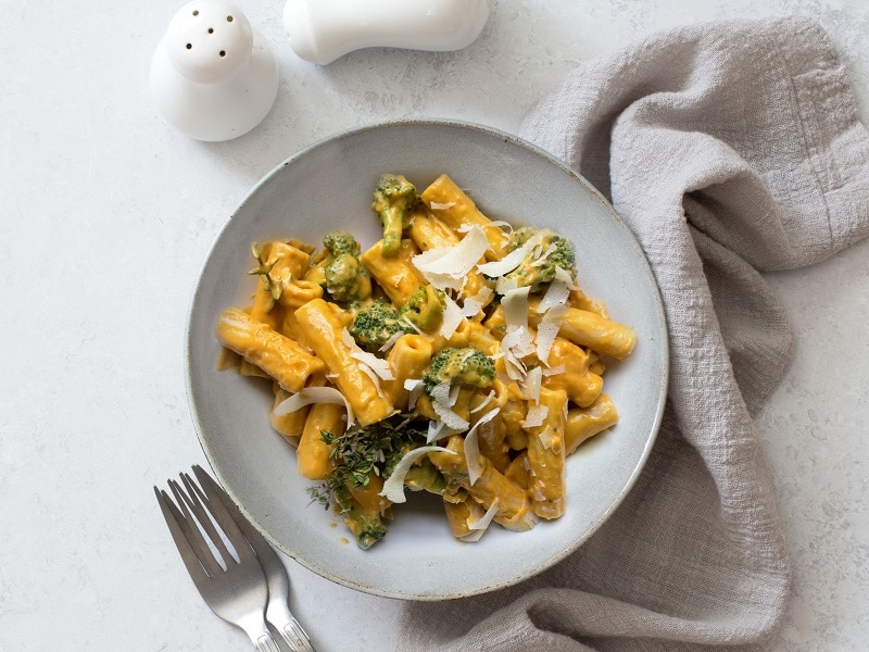 An Overhead View Shows Pumpkin Alfredo Sauce Over Penne and Broccoli in a White Bowl.