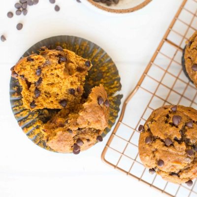 Vegan Pumpkin Muffins With Chocolate Chips Sit on a Cooling Rack With One Split Open to Reveal Mini Chocolate Chips inside an Orange, Cakey Muffin.
