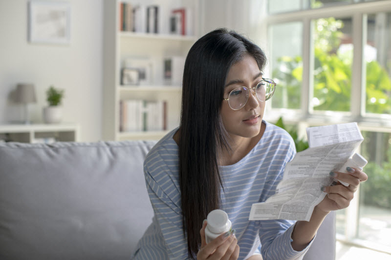 Woman Reading Vitamin-Level Testing Results on Couch While Holding Bottle of Supplements