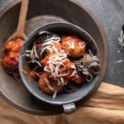 Spooky-Looking Black Bean Spaghetti and Meatballs with Shredded Mozzarella Cheese in Black Bowl on Slate Countertop