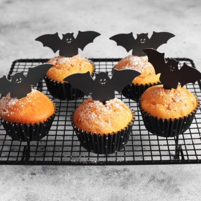 Halloween Chai Muffins in Black Paper Cupcake Cups on Black Wire Rack on Grey Background. Spooky and Cute Paper Bats are Flying Up off Toothpicks on Each.