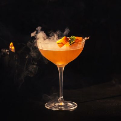 Eerie Halloween Cocktail in Martini Glass With Dry Ice shown on Black Background with Flickering Candle Flame