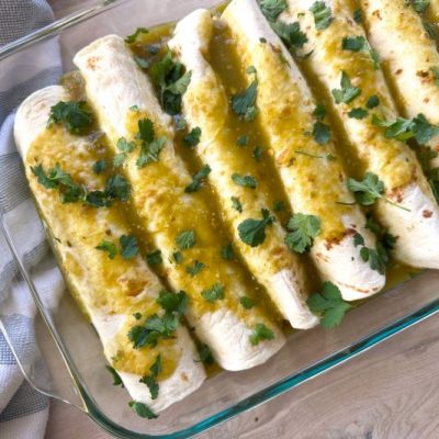 Vegan Enchiladas Lined Up in a Glass Baking Dish Covered in Green Chili Sauce and Sprinkles of Cilantro