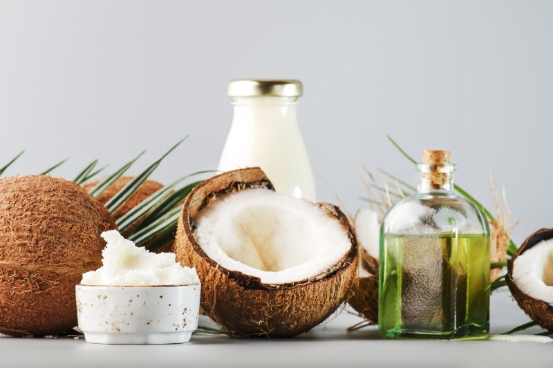 Uses for Coconut Oil Concept Represented by Half-Open Coconut and Coconut Oil in Bottles and Dish on White Surface