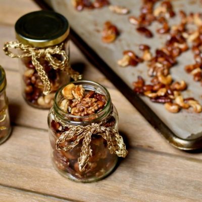 Roasted Nuts in Mason Jars Decorated with Ribbon Next to Sheet Pan with Mixed Nuts