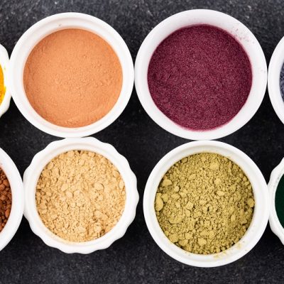An Overhead View Shows A Cluster of Small White Bowls Filled With Colorful Powdered Spices and Superfoods, Representing How to Make Eyeshadow.