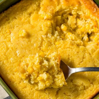Vegan Corn Casserole in Square Baking Dish With Serving Spoon Scooping It Up