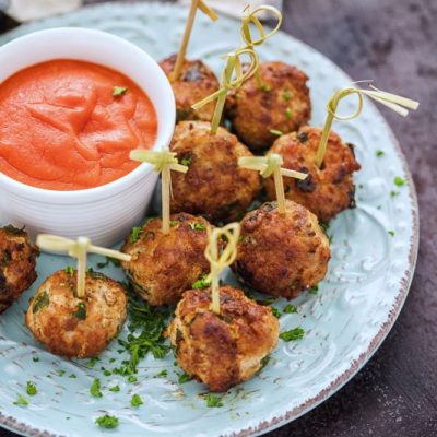 Plant-Based Chickpea Meatballs on Tied Bamboo Skewers Arranged on White Earthenware Plate with a Small Bowl of Marinara Dipping Sauce