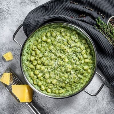 Superfood Pesto Gnocchi in a Pot Next to a Block of Parmesan Cheese