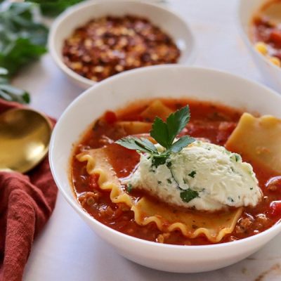 A White Bowl Shows a Lasagna Soup Recipe With Tomato Broth, Lasagna Noodles and a Generous Dollop of Ricotta With Parsley.