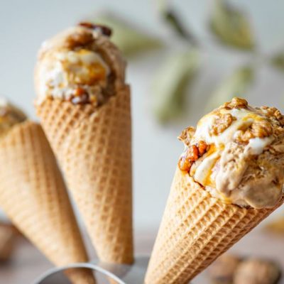 Three Ice Cream Cones Each Filled with a Scoop of Maple Walnut Ice Cream Drizzled with Caramel Sauce and Topped with Walnut Pieces