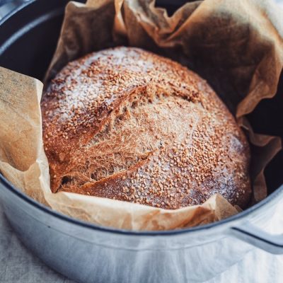 A No Knead Whole Wheat Bread is in a Cast-Iron Dutch Oven, Topped With Sesame Seeds.