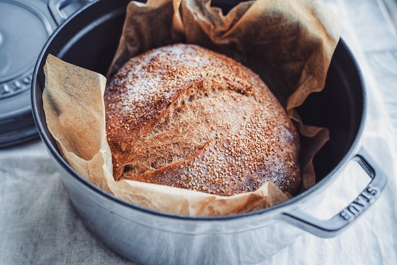A No Knead Whole Wheat Bread is in a Cast-Iron Dutch Oven, Topped With Sesame Seeds.