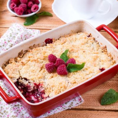 Raspberry Crumble in Red Baking Dish on Rustic Wooden Surface