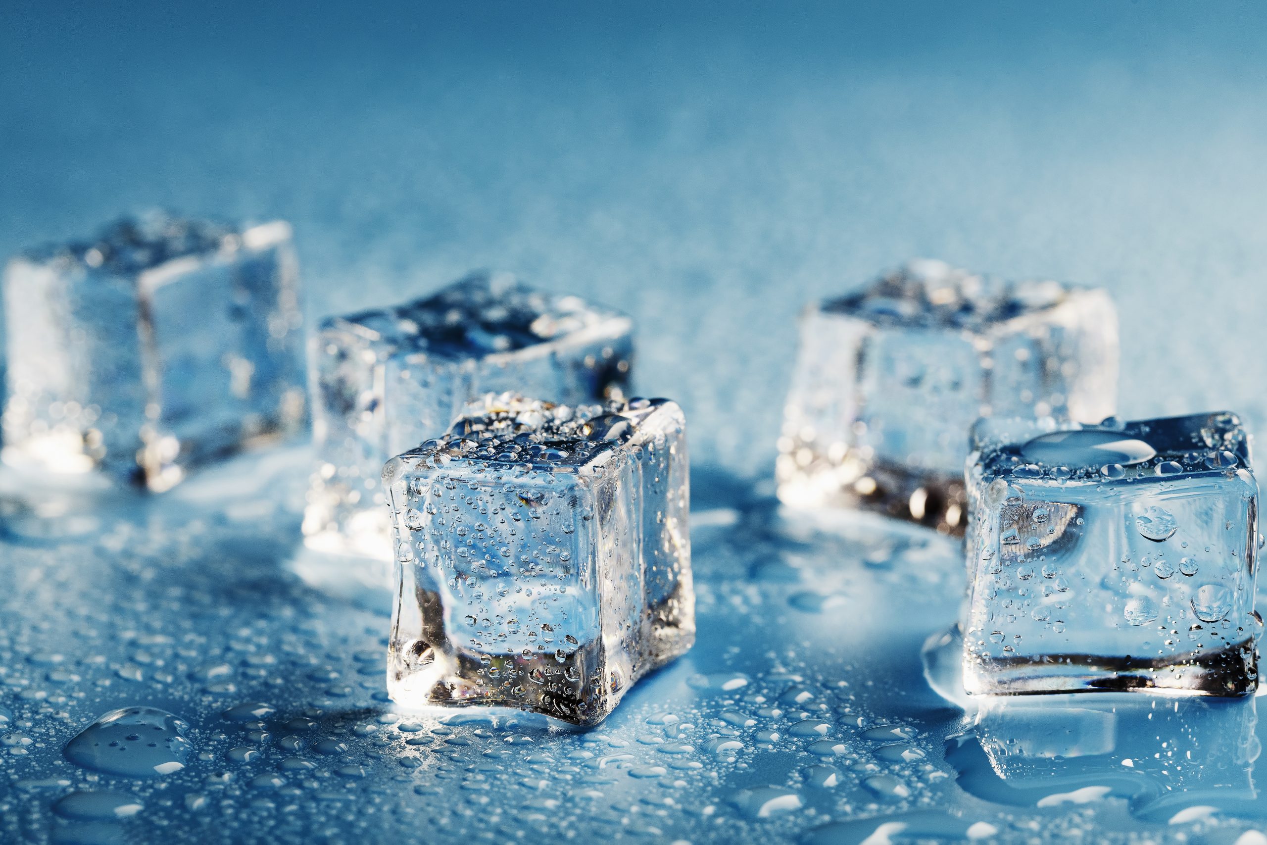 Close-up ice cubes with melt water drops scattered on aa blue background. Macro. Refreshing ice for drinks and cocktails on a hot, sultry day.