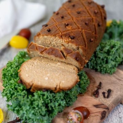 Glazed Baked Vegan Ham on Wooden Cutting Board Surrounded by Fresh Vegetables