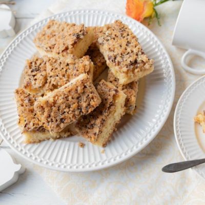 Slices of Hazelnut Cake with Caramel Cookie Crumble on Fancy, Ridged Plate Surrounded by Strewn Roses and Easter Bunny Decorations