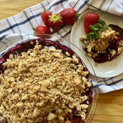 Berry Rhubarb Crisp With Hibiscus in Glass Pie Pan Next to Plate With a Big Serving