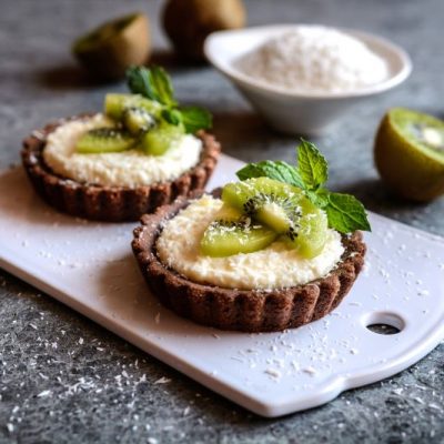 Cashew-Coconut Cream & Kiwi Chocolate Tarts on Cutting Board Surrounded by Sliced Kiwis