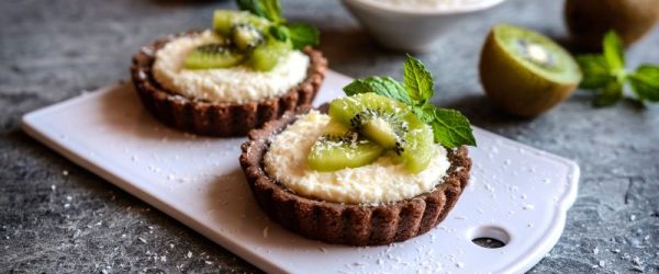 Cashew-Coconut Cream & Kiwi Chocolate Tarts on Cutting Board Surrounded by Sliced Kiwis