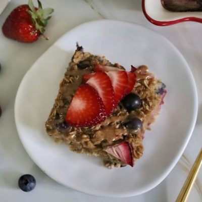 Overhead Shot of Berry Baked Oatmeal on an Oblong White Plate Next to a Gold Fork