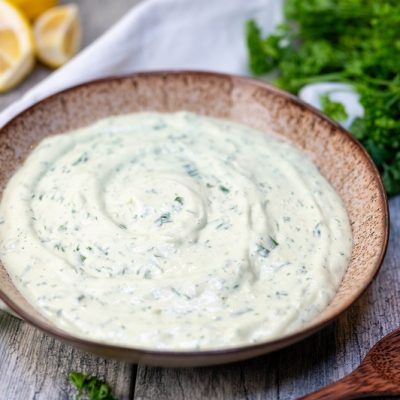 A Brown Bowl is Filled With Creamy Green Goddess Dip and Surrounded by Curly Parsley and Lemon Wedges.