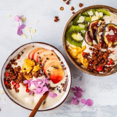 Overhead Photo of Two Protein-Packed Fruit Smoothie Bowls Topped with Slices of Fig and Kiwi with Sprinkling of Goldenberries and Cacao Nibs