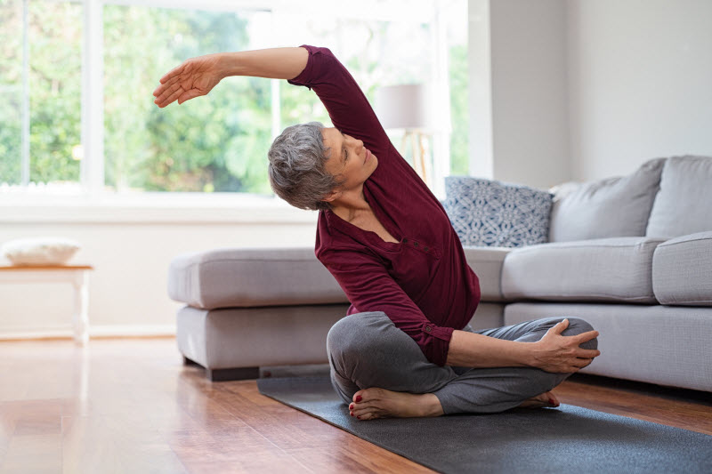 Mature Woman in Living Room on Yoga Mat Using Stretching as One of the Ways to Lower Blood Pressure