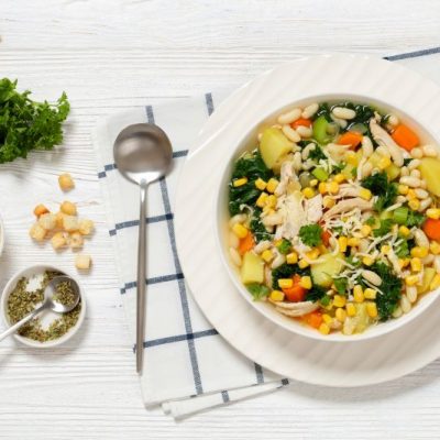 Overhead shot of Vegetable-Filled Chicken & White Bean Soup in a Big Soup Bowl on White Wooden Table