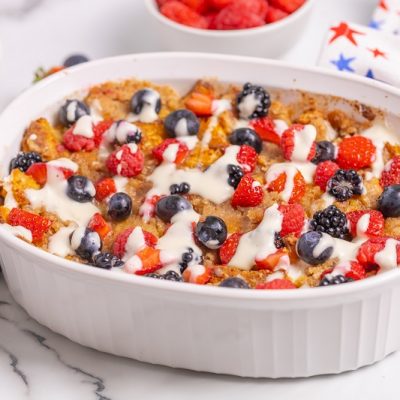 A Gluten Free French Toast Casserole Is Covered in Blue and Red Berries With a White Cream Cheese Glaze, Making It Perfect for a Fourth of July Gathering.