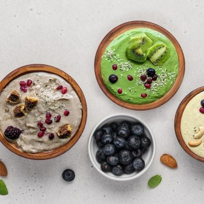 An Overhead View of Three Colorful Magnesium Smoothie Bowls Surrounded by Fruits and Nuts.