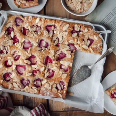 Strawberry Sheet Cake Topped with Slices of Strawberries & Almonds in Sheet Pan on Wooden Tabletop