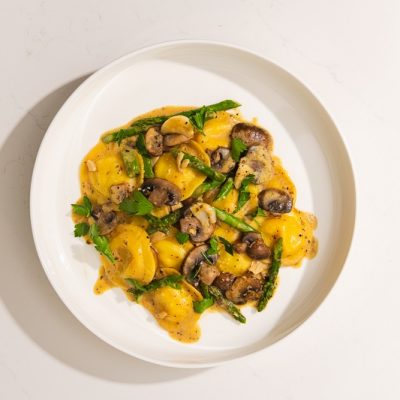 A White Rimmed Plate Has a Serving of Ravioli and Asparagus in a Creamy Mushroom Sauce.