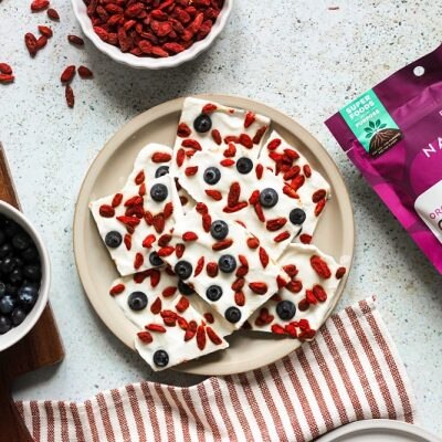 Greek Yogurt Bark With Goji Berries and Blueberries is Displayed On a Plate Surrounded by Navitas Organics Superfood Ingredients.