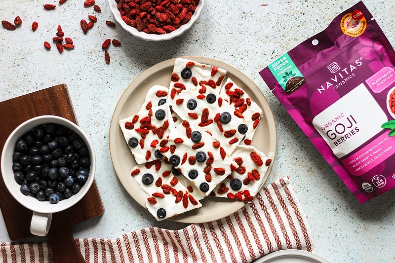 Greek Yogurt Bark With Goji Berries and Blueberries is Displayed On a Plate Surrounded by Navitas Organics Superfood Ingredients.