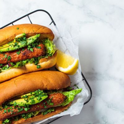 Grilled Carrot Hot Dogs with Spicy Cilantro Sauce in Toasted Buns With Sliced Avocado, Romaine Leaves and Wedge of Lime