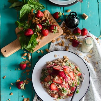 A Bowl of Summer Farro Salad With Strawberries and Basil Sit on a Wooden Table.