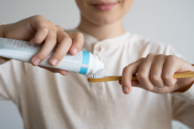 What Causes Bad Breath? Top Reasons & Tips to Stay Fresh Smiling Woman Applying Toothpaste to Bamboo Toothbrush to Represent Concept of What Causes Bad Breath