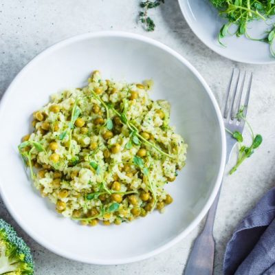 Broccoli & Pea Risotto in Round White Bowl Next to a Fork and a Plate Filled With Broccoli Sprouts