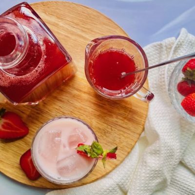 Strawberry Syrup in Glass Decanter Next to Glass of Strawberry Milk With Ice and Sliced Strawberries