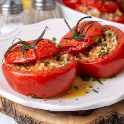 Stuffed Tomatoes Filled With Rice and Herbs on Scallop-Edged White Plate Set on Rustic Wooden Board
