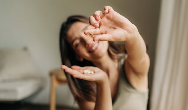 Smiling Woman Holding Supplement Gel Capsules in Her Hands to Represent Concept of Best Hair Supplements