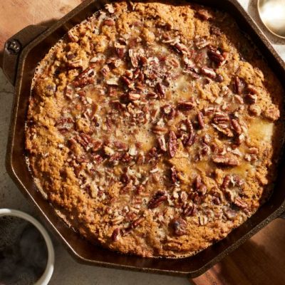 Pecan & Pumpkin Pie Skillet Cookie in Octagonal Cast Iron Skillet on Earthy Tabletop, with Mugs Full of Warm Coffee Nearby