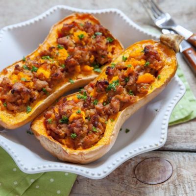 Stuffed Butternut Squash With Beef & Broccoli in Scallop-Edged White Dish on Wooden Table Set With Horn-Handled Flatware