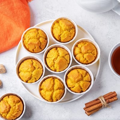 Eight Golden Milk Muffins Sit Beside a Cup of Tea, Three Sugar Cubes and a Bundle of Cinnamon Sticks.