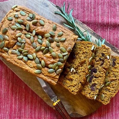 Savory Sweet Potato Bread With Pumpkin Seeds on Top on a Wooden Cutting Board Next to a Sprig of Rosemary