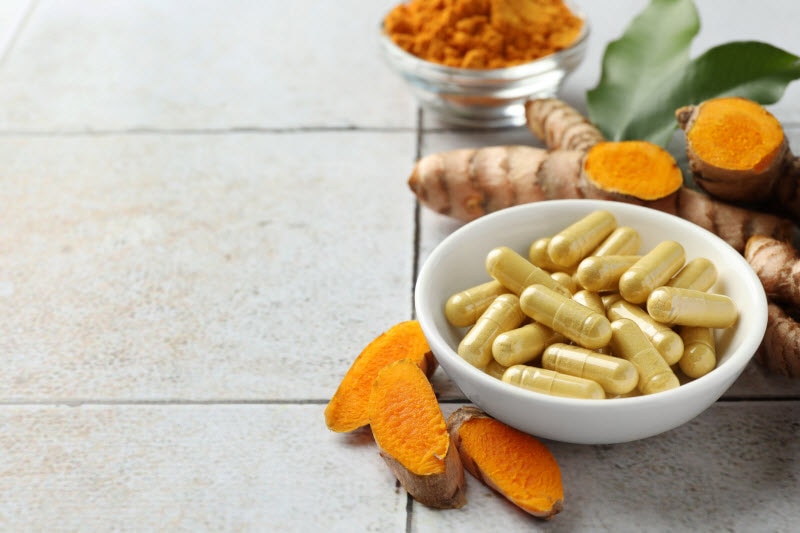 Bowl of Turmeric Capsules with Fresh Turmeric and Leaves to Represent Concept of Supplements and Liver Toxicity
