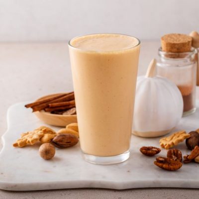 Vegan Pumpkin Spice Milk in Tall Glass on Marble Cutting Board Strewn with Nuts, Cookies and Cinnamon Sticks